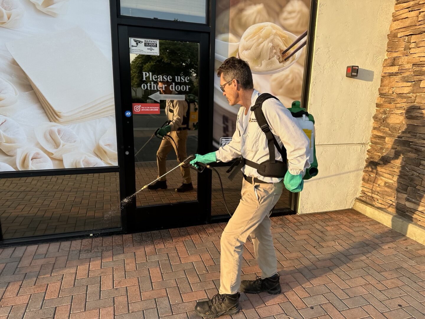 A man in white shirt and green gloves holding a mop.